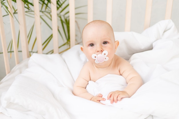 Bambina con un ciuccio in una culla su un letto di cotone bianco di sei mesi