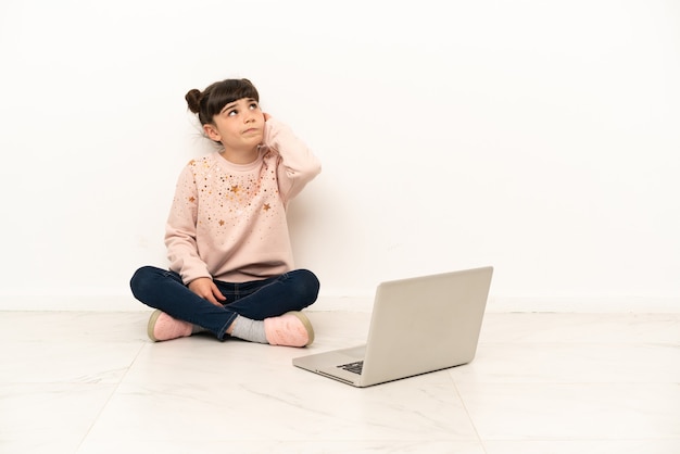 Bambina con un computer portatile che si siede sul pavimento che ha dubbi