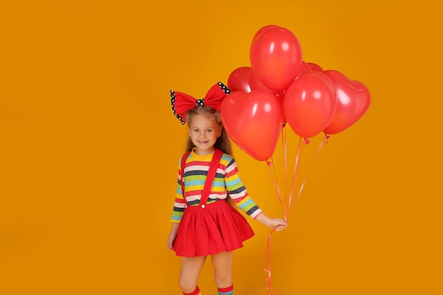 bambina con un fiocco in testa in una maglietta colorata con una gonna rossa tiene dei palloncini nelle sue mani