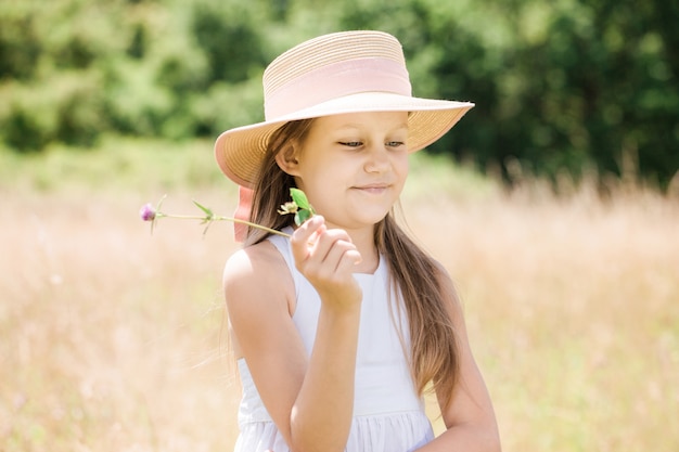 Bambina con un fiore di trifoglio in un cappello nel prato