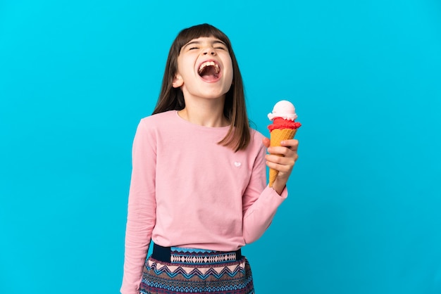 Bambina con un gelato alla cornetta isolato su sfondo blu ridendo