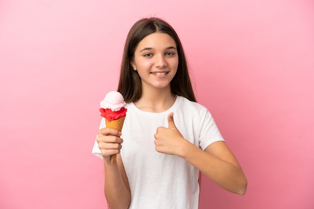 Bambina con un gelato alla cornetta su sfondo rosa isolato che fa un gesto di pollice in alto