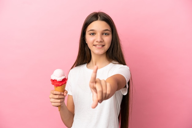 Bambina con un gelato alla cornetta su sfondo rosa isolato che mostra e solleva un dito