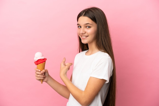 Bambina con un gelato alla cornetta su sfondo rosa isolato che punta indietro