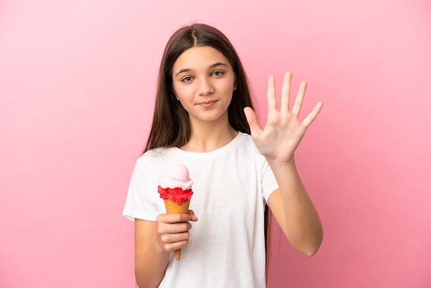 Bambina con un gelato alla cornetta su sfondo rosa isolato contando cinque con le dita