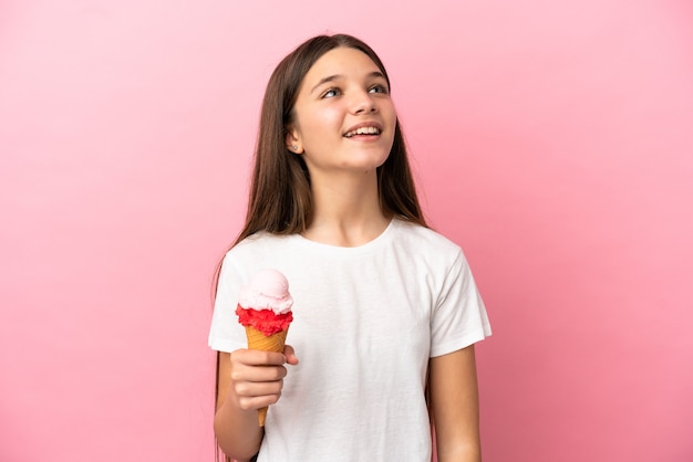 Bambina con un gelato alla cornetta su sfondo rosa isolato ridendo