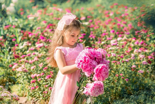 Bambina con un grande mazzo di peonie. Un bambino cammina nel parco con i fiori in estate.