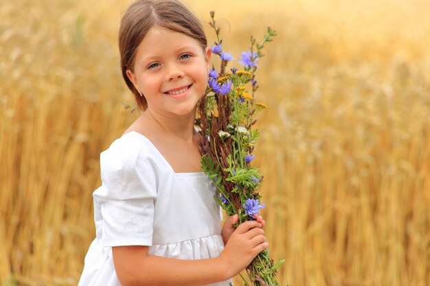 Bambina con un mazzo di fiori di campo sul campo