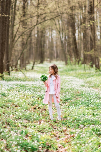 Bambina con un mazzo di primule nella foresta primaverile.