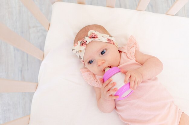 Bambina con una bottiglia di latte in mano su un letto di cotone bianco a casa, il concetto di alimentazione sana dei bambini