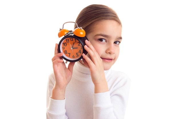 Bambina con una lunga coda di cavallo castagna che nasconde il viso oltre l'orologio arancione su sfondo bianco