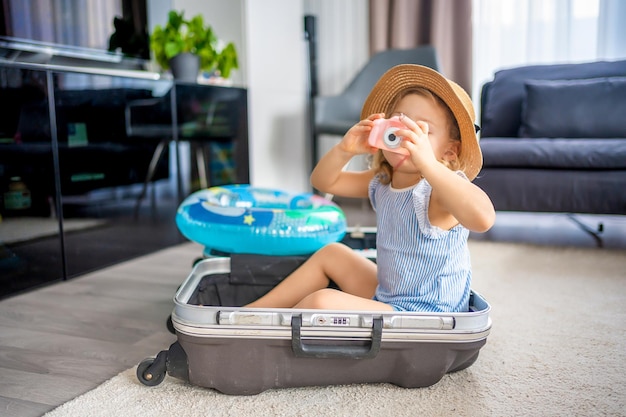 Bambina con valigia bagaglio bagaglio e salvagente gonfiabile che gioca con la fotocamera giocattolo e pronto