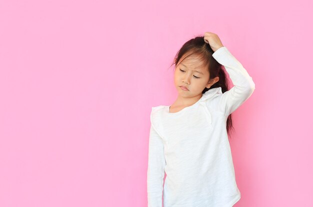 Bambina confusa graffiando la sua testa su sfondo rosa