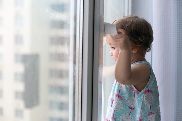 Bambina contro la finestra chiusa che guarda fuori.