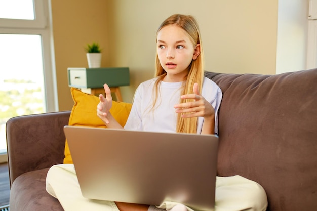 Bambina dai capelli biondi che usa un laptop che fa i compiti a casa Torna al concetto di scuola