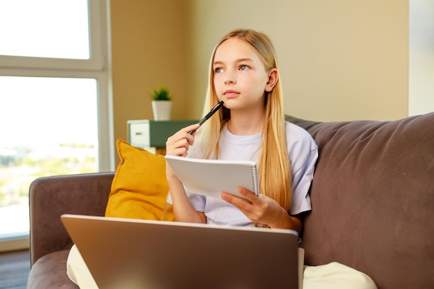 Bambina dai capelli biondi che usa un laptop che fa i compiti a casa Torna al concetto di scuola