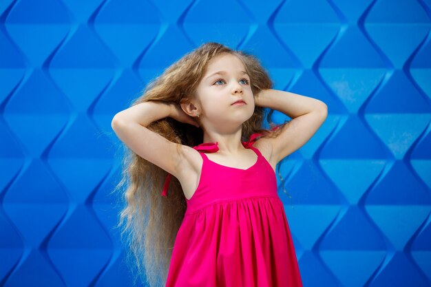 Bambina dai capelli biondi in un vestito rosa su uno sfondo blu che balla e ride, emozioni di gioia per bambini brillanti, infanzia felice