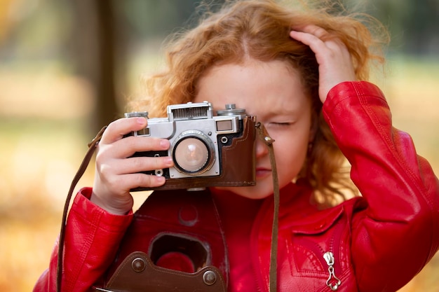 Bambina dai capelli rossi con una fotocamera retrò su uno sfondo autunnale