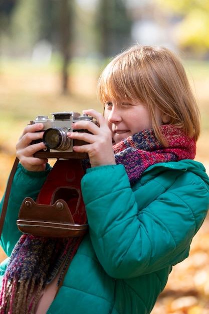 Bambina dai capelli rossi con una macchina fotografica retrò nel parco in autunno Bambino fotografo