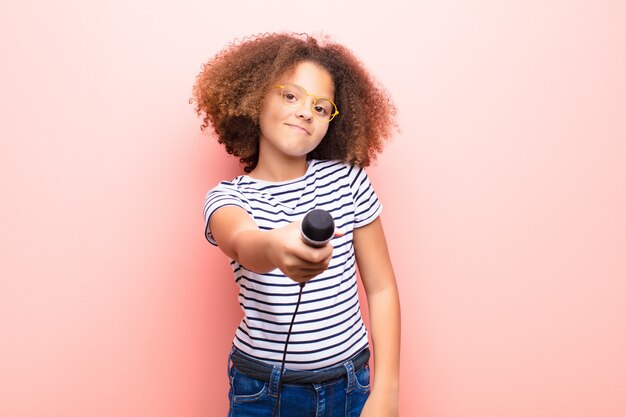 Bambina dell'afroamericano contro la parete piana con un microfono