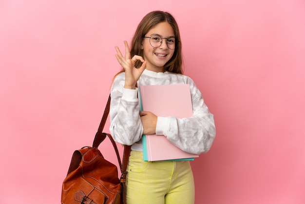 Bambina dell'allievo sopra la parete rosa isolata che mostra segno giusto con le dita