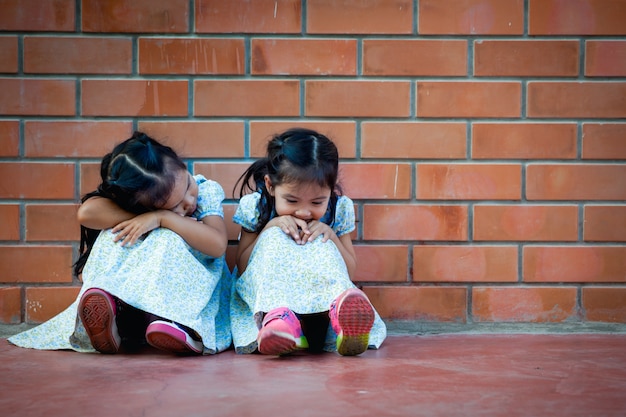 Bambina dell&#39;Asia che si siede con l&#39;amico sul fondo del muro di mattoni