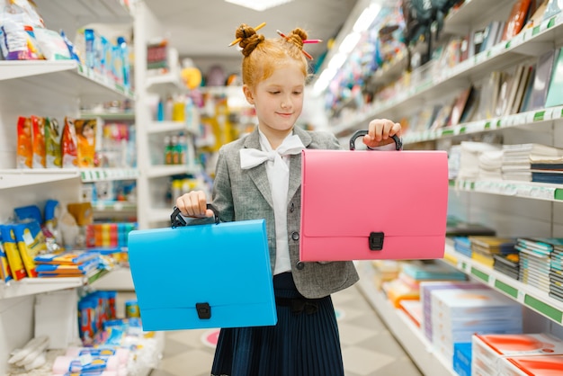 Bambina della scuola con due cartelle in cartoleria. Bambina che compra forniture per ufficio in negozio, scolaretta al supermercato