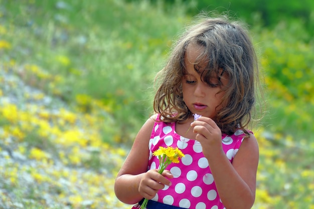 Bambina dentro su un giacimento di fiore con un mazzo di fiori gialli