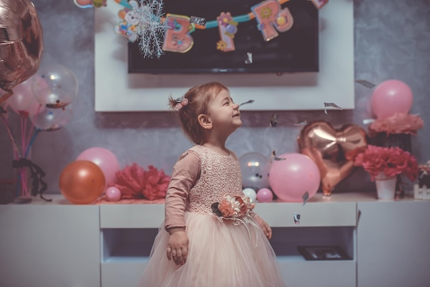 Bambina di 2 anni in abito rosa con la sua prima torta di compleanno carda di buon compleanno la bambina carina festeggia il suo primo compleanno circondata da regali