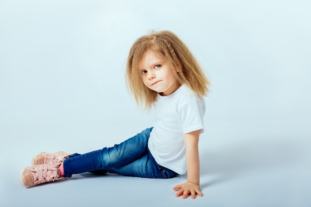 Bambina di 4 anni con i capelli ricci che indossa camicia bianca, blue jeans, stivali rosa seduti sul pavimento, sorridenti e alla ricerca