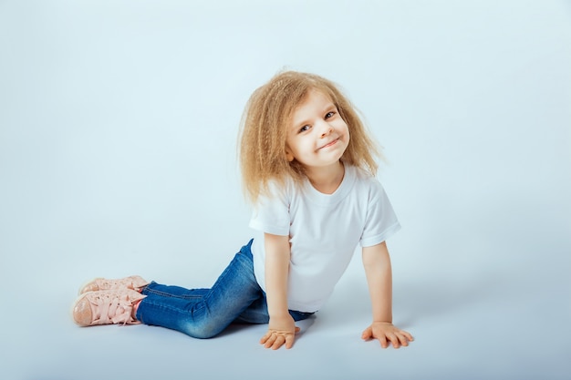 Bambina di 4 anni con i capelli ricci che indossa camicia bianca, blue jeans, stivali rosa seduti sul pavimento, sorridenti e alla ricerca