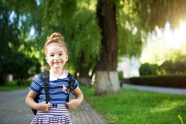 bambina di aspetto caucasico in uniforme scolastica con uno zaino. Concetto torna a scuola. Scuola elementare, sviluppo di attività per bambini in età prescolare.