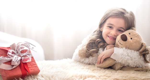 Bambina di concetto di natale che abbraccia il giocattolo dell'orso