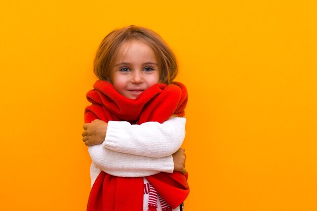 Bambina divertente che fa capolino da dietro una sciarpa rossa su uno sfondo giallo isolato a natale