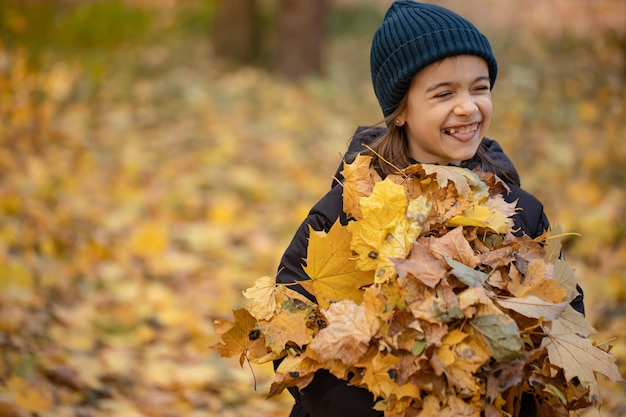 Bambina divertente che tiene un mazzo di foglie di autunno nella foresta