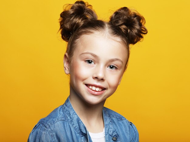 Bambina divertente con capelli ricci biondi che ride guardando a porte chiuse con espressione soddisfatta su sfondo giallo