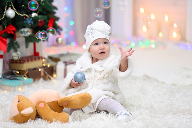 Bambina divertente con il giocattolo di Natale vicino all'albero di Natale su sfondo luminoso bright