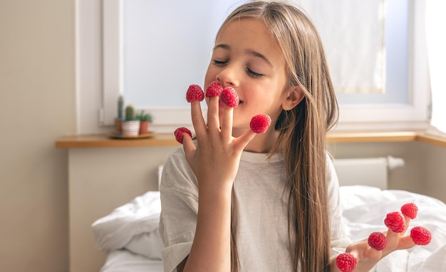 Bambina divertente con lamponi sulle dita a letto al mattino