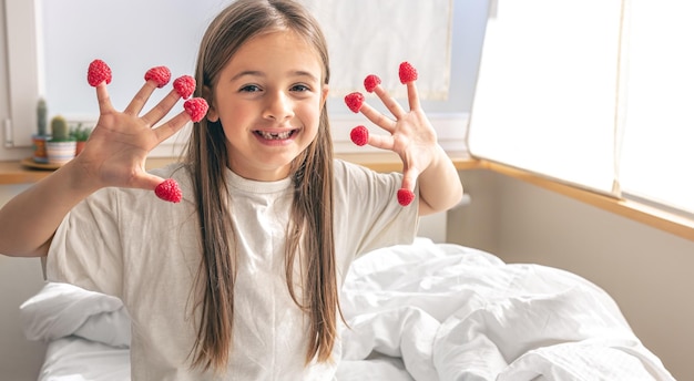 Bambina divertente con lamponi sulle dita a letto al mattino