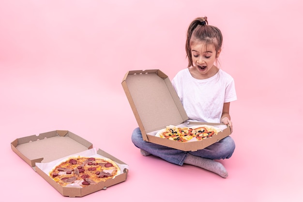 Bambina divertente deliziata con la pizza in una scatola per la consegna, sfondo rosa.