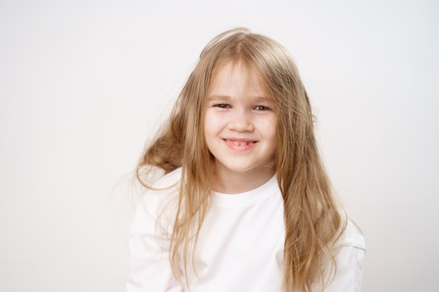 Bambina divertente e carina con i capelli lunghi arruffati su bianco.