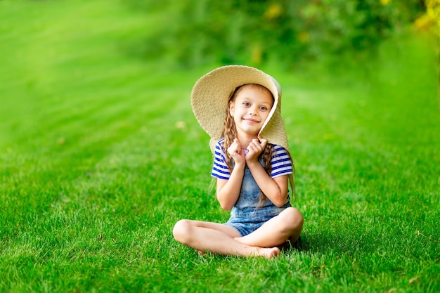 Bambina divertente in estate sul prato con un grande cappello di paglia sull'erba verde che si diverte e si rallegra, spazio per il testo