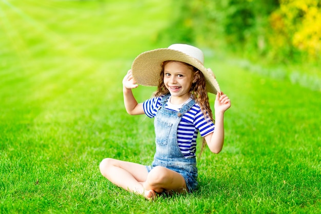 Bambina divertente in estate sul prato con un grande cappello di paglia sull'erba verde che si diverte e si rallegra, spazio per il testo
