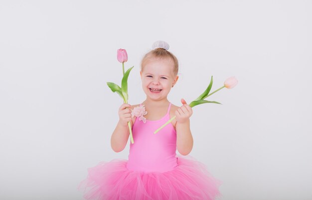 Bambina divertente in un vestito rosa con i tulipani su una parete bianca