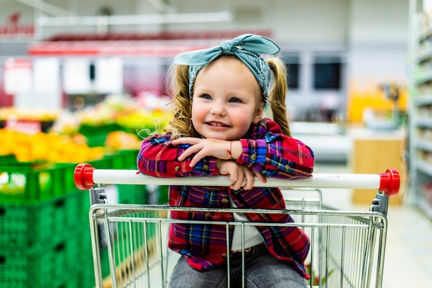 Bambina divertente, seduta nel carrello durante la spesa in famiglia nell'ipermercato