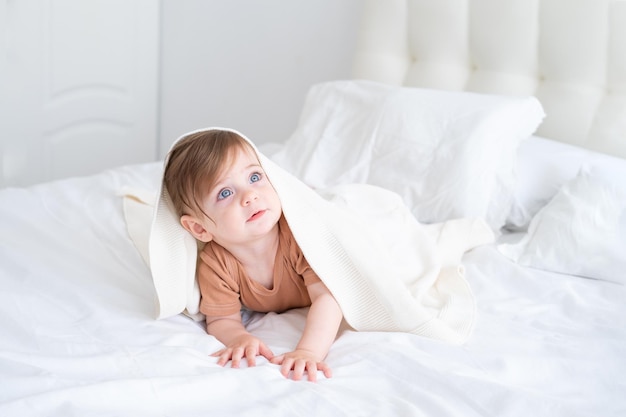 bambina divertente sorridente e sdraiata su un lino bianco sotto la coperta a casa