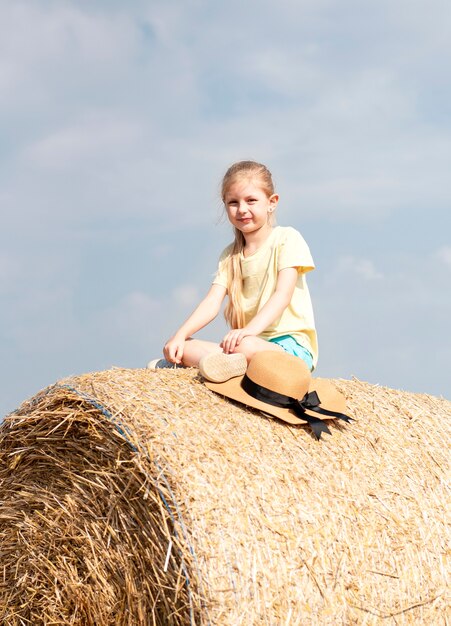 Bambina divertirsi in un campo di grano in una giornata estiva. Bambino che gioca al campo di balle di fieno durante il periodo del raccolto.