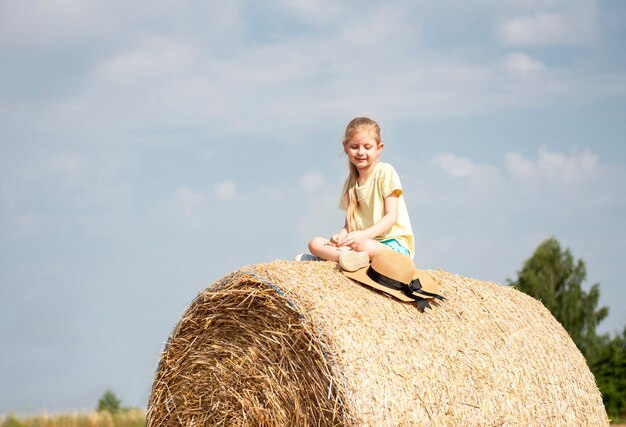 Bambina divertirsi in un campo di grano in una giornata estiva. Bambino che gioca al campo di balle di fieno durante il periodo del raccolto.