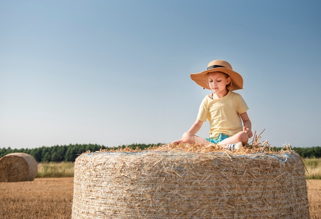 Bambina divertirsi in un campo di grano in una giornata estiva. Bambino che gioca al campo di balle di fieno durante il periodo del raccolto.