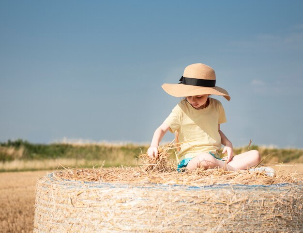 Bambina divertirsi in un campo di grano in una giornata estiva. Bambino che gioca al campo di balle di fieno durante il periodo del raccolto.